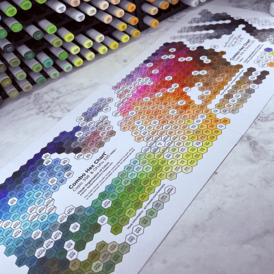 A color chart filled in with alcohol markers on a white desk.